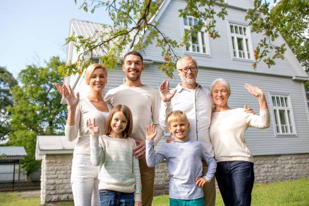 family, generation, gesture, home and people concept - happy family standing in front of house waving hands outdoors